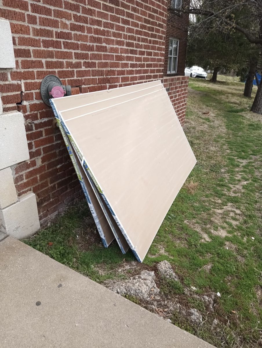 Scrap drywall leaning against a brick house